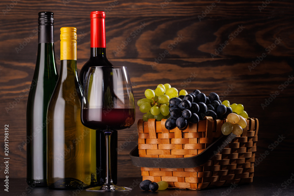 Obraz premium Red and white wine bottles with a glass and basket of fresh grapes