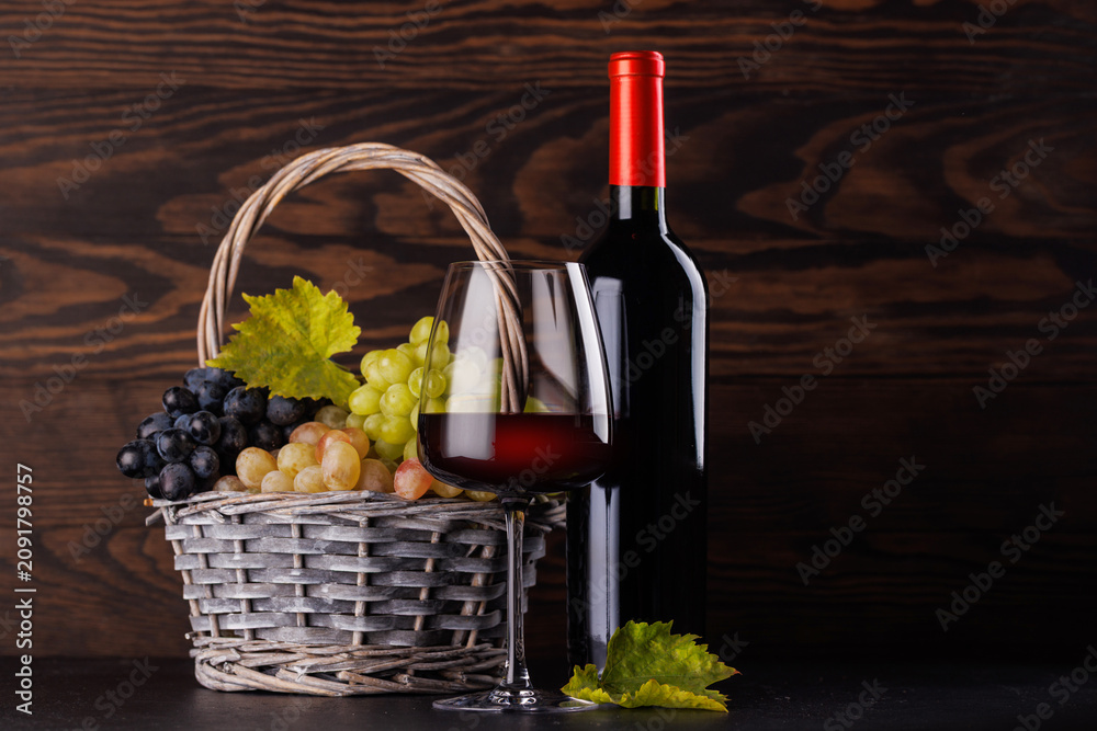 Obraz premium Red wine bottle with a glass and basket of fresh grapes
