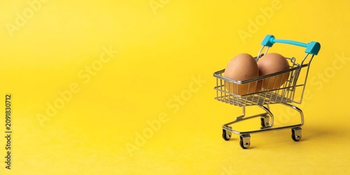 Shopping cart with egg on yellow background, grocery shopping and food price concept