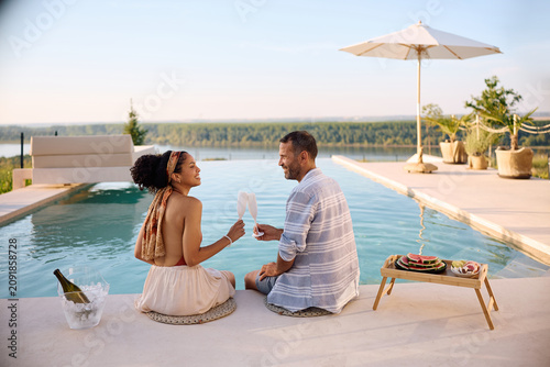 Carefree couple toasting with champagne while relaxing by the infinity pool on summer vacation.