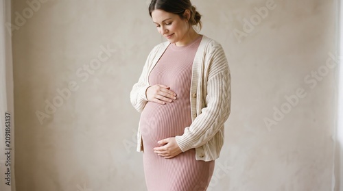 Pregnant woman in cozy outfit gently touching her belly indoors
