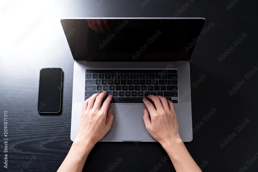 Fototapeta premium Hands Typing on Laptop with Smartphone Nearby