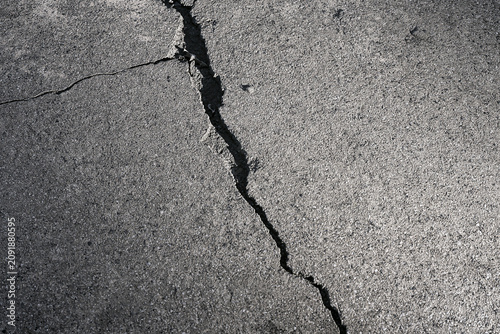 Top view of a deep long crack across a grey asphalt surface
