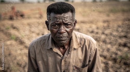 Elderly African Farmer Portrait Standing in a Dry Arid Farm Field During Drought Conditions Reflecting Poverty Hardship and Agricultural Challenges for Smallholder Rural Subsistence Growers