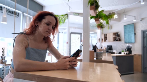 A teenage girl, a blogger, uses a mobile phone while sitting in a cafe.