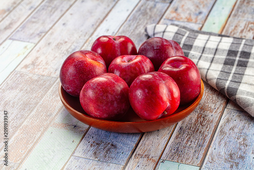 Принти на полотні Red plums in wooden bowl on rustic painted wood table with checkered cloth