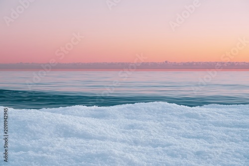 Arctic ice shore resting against calm ocean water under a pink pastel sunset with sharp focus for winter travel and environmental marketing