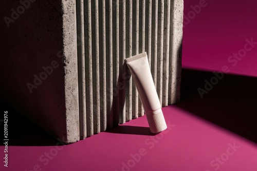 Cosmetic tube mockup leaning against ribbed concrete block with dramatic shadows on magenta background for luxury beauty branding