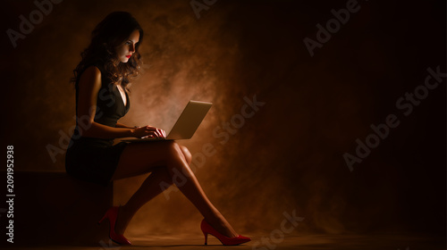 Young woman works on laptop in a dimly lit room with a warm atmosphere during evening hours
