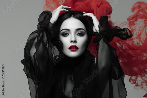 Woman poses with black fabric and red smoke in studio setting during a photoshoot in the evening light