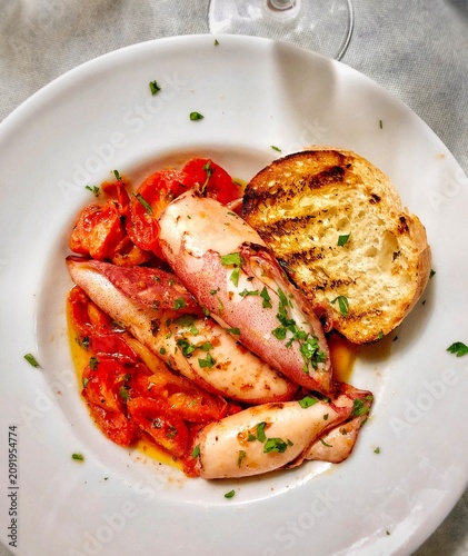 Squid with tomato sauce with bread on plate authentic Italian trattoria food.