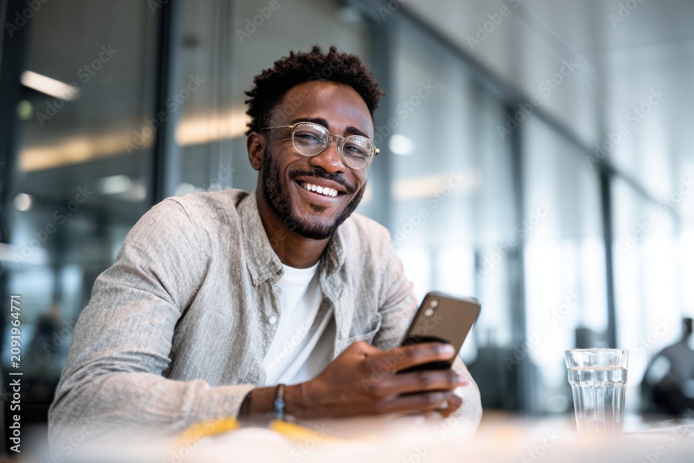 Fototapeta premium Happy young professional talking on a smartphone in a modern office, representing business communication, customer service, remote work, and positive workplace interactions.