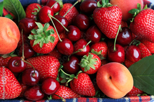 Fresh strawberries and cherries with a peach on a blue basket during summer harvest season
