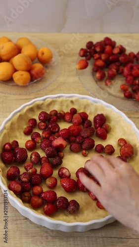 Woman's hands placing fresh strawberries on raw dough in a baking dish while preparing a pie