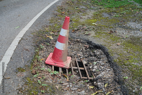 Red and white traffic cone marking uncovered metal grate near road edge