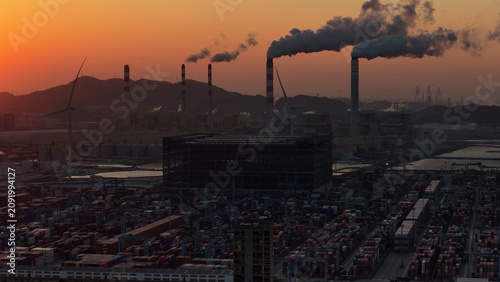 Industrial port area large shipping cargo containers sunset. Fossil fuel power plant air smoke stacks, wind turbine. Global logistics trade industry terminal. Windmill energy factory. Smoking chimneys
