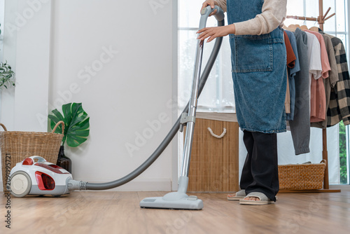 Vacuum cleaner housework cleaning home floor person denim apron living room appliance hose with calm adult using canister vacuum on wood floor near clothing rack