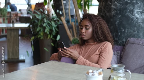 Cute African American woman using a mobile phone in a cafe