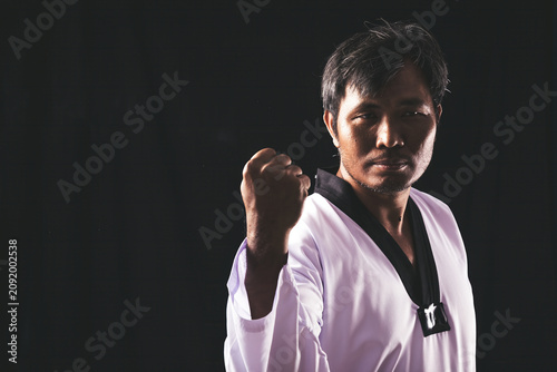 Cuadro en lienzo A focused martial artist in a taekwondo uniform raises a clenched fist against a