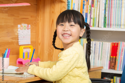 Quadro su tela diligent primary student girl writing in her notebook with a pencil, doing homework at home desk