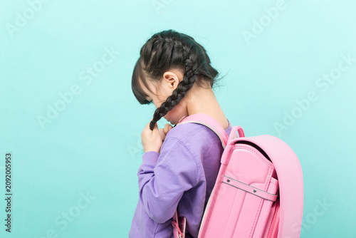 фотографія An anxious Asian girl is seen fidgeting with her braids, looking down and displaying nervousness – a sign of back-to-school anxiety and childhood stress
