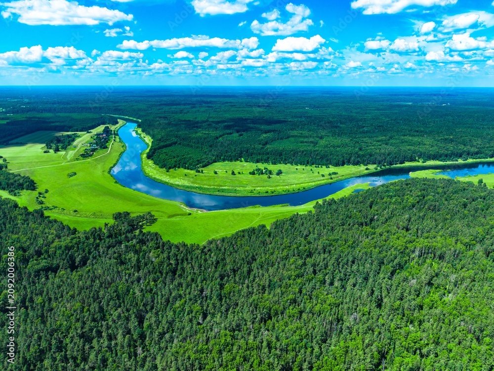 Naklejka premium Riverbank with lush green trees and vibrant blue waters under a clear sunny sky with clouds