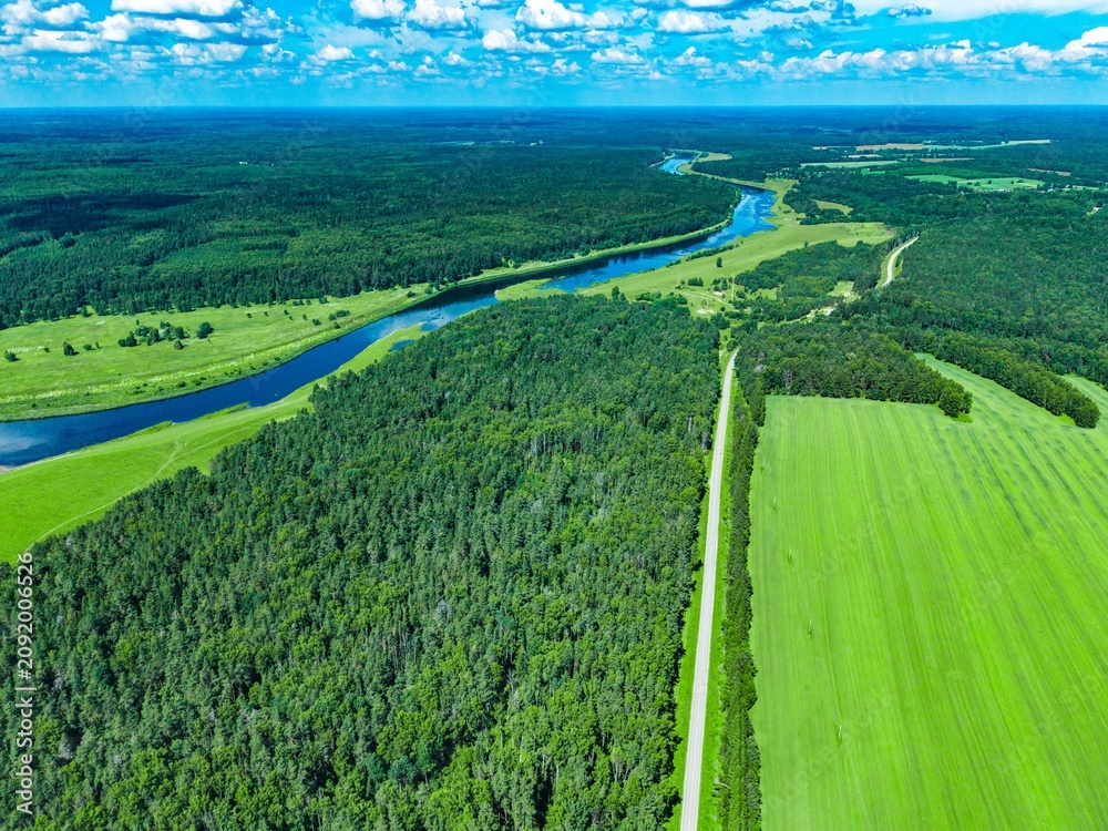 Obraz premium Aerial view of lush green fields and winding river meandering through dense forest landscape