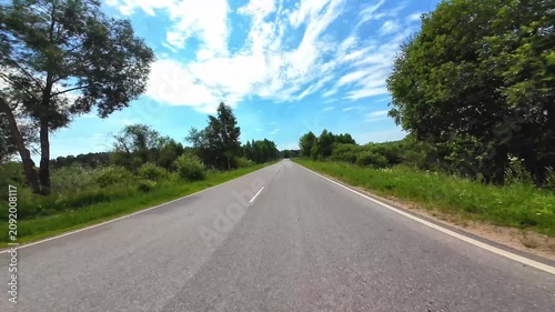 Asphalt road stretching through green foliage under a bright blue sky in summer scenery