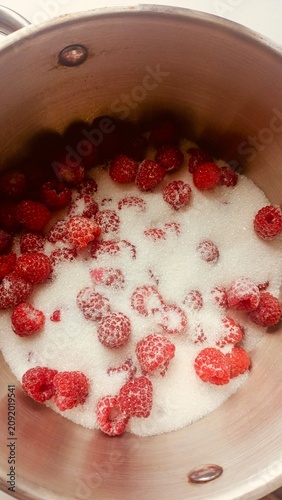 Top-down view of fresh red raspberries and white granulated sugar inside a stainless steel cooking pot, ready for making jam.