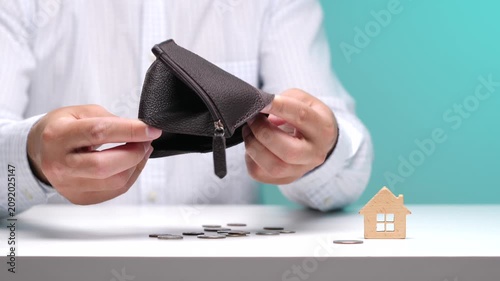 Person's hands holding an empty leather wallet with very few coins and a small wooden house model on a table, symbolizing financial crisis, budget issues, and housing affordability problems