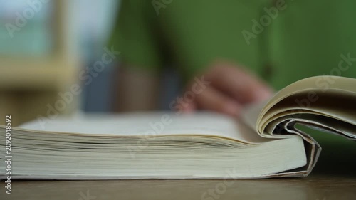 Close-up of female hands turning page book. Unrecognizable Person's Hand reading a book and holding fingers along the lines. Concept for reading, studying, research, education.