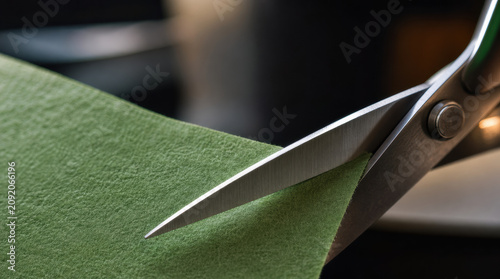 Sharp scissors metallic blade green fabric cutting close up texture craft tool tailor Metal scissor cutting green textured fabric with sharp blade close up view, craft detail for sewing, tailoring