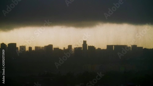 Dramatic and beautiful shot of dark clouds gathering over the modern cityscape, silhouetted against the sunrise, as monsoon rain showers over city skyline. Cinematic urban landscape of Mumbai, India