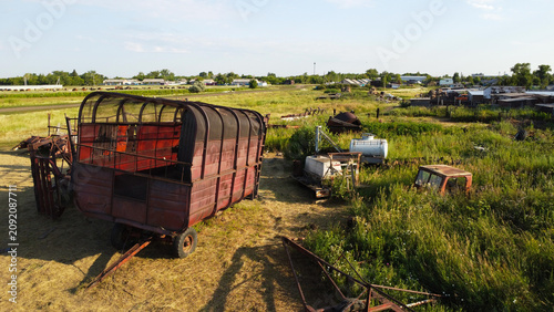 Fotografie Old rusty agricultural trailers and scrapped farm machinery parts sitting in a grassy field yard