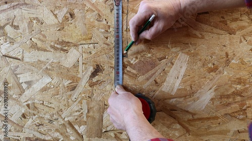 фотографія The hands of a craftsman marking out the OSB board