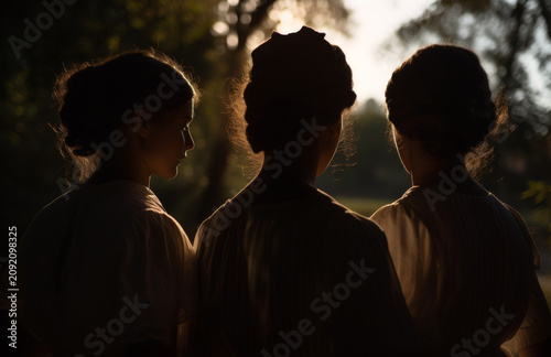 Three silhouetted women standing together at sunset in a park