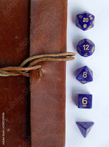Konstfotografi Purple gaming dice lined up next to a vintage leather journal on a white backgro