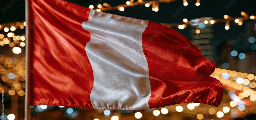 Fototapeta premium At night in a lively city, the Peruvian flag waves proudly, symbolizing national pride and cultural celebration.
