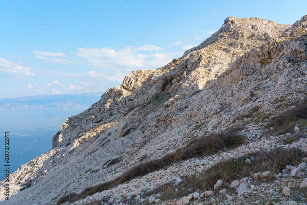 Fototapeta premium A rugged limestone mountain ridge rises above the crystal-blue Adriatic Sea under a clear sky on the Croatian coast