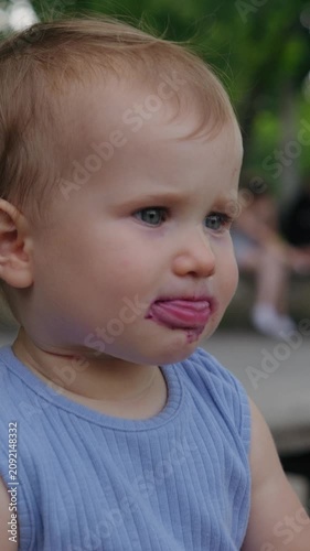 Close-up of a cute toddler eating purple ice cream from a waffle cone in a park, vertical video.