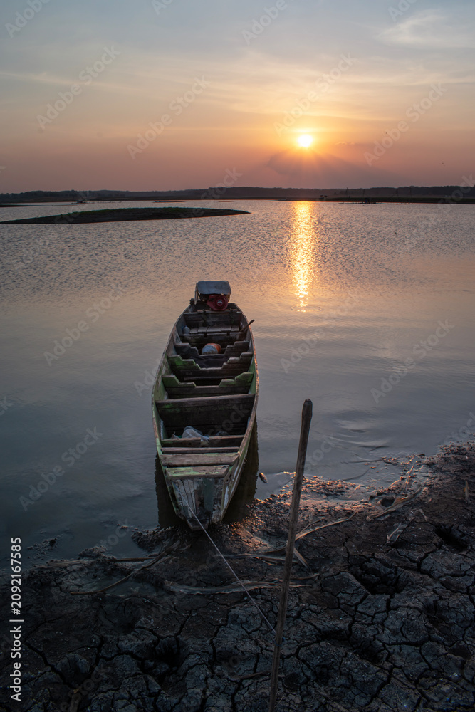 Obraz premium A fisherman's boat rests at the lake's edge at sunset, a small wooden boat on the dry lakeshore.