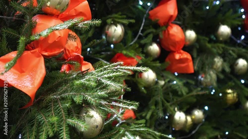 Christmas tree outdoors adorned with vibrant baubles, ribbons, and lights. The evergreen branches hold red and gold ornaments, enhancing the festive holiday ambiance.