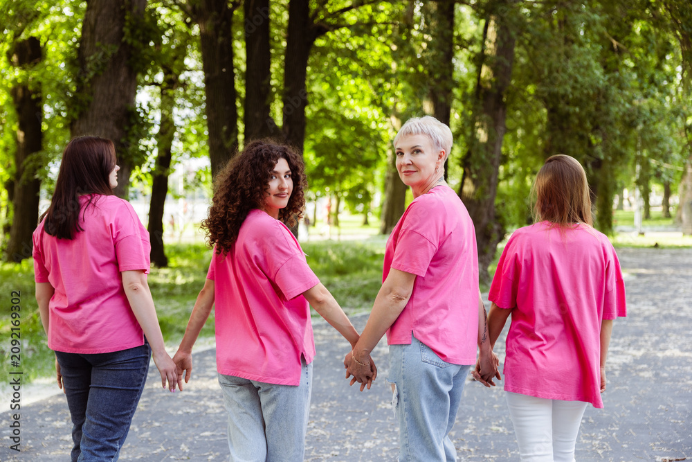 Fototapeta premium Women wearing pink t shirts walking holding hands in park