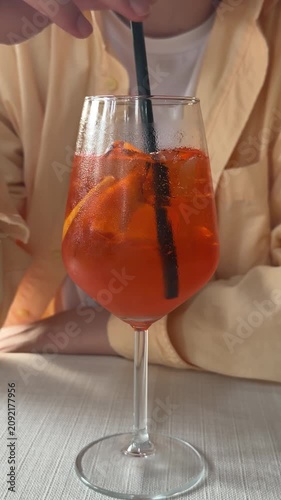 Glass of Aperol spritz cocktail with black straw on restaurant table, refreshing orange summer drink for outdoor cafe, social dining and relaxed evening atmosphere