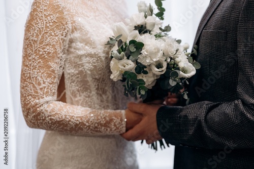 Fotografie Bride and groom holding hands with a white rose and eucalyptus wedding bouquet