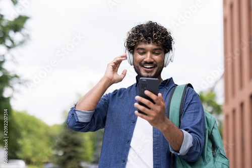 Obraz na płótnie Happy young man with curly hair wearing headphones and a backpack, listening to