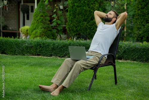 Adult man relaxing in a garden chair with a laptop after completing work tasks. Remote work lifestyle, stress-free productivity, work-life balance, outdoor office