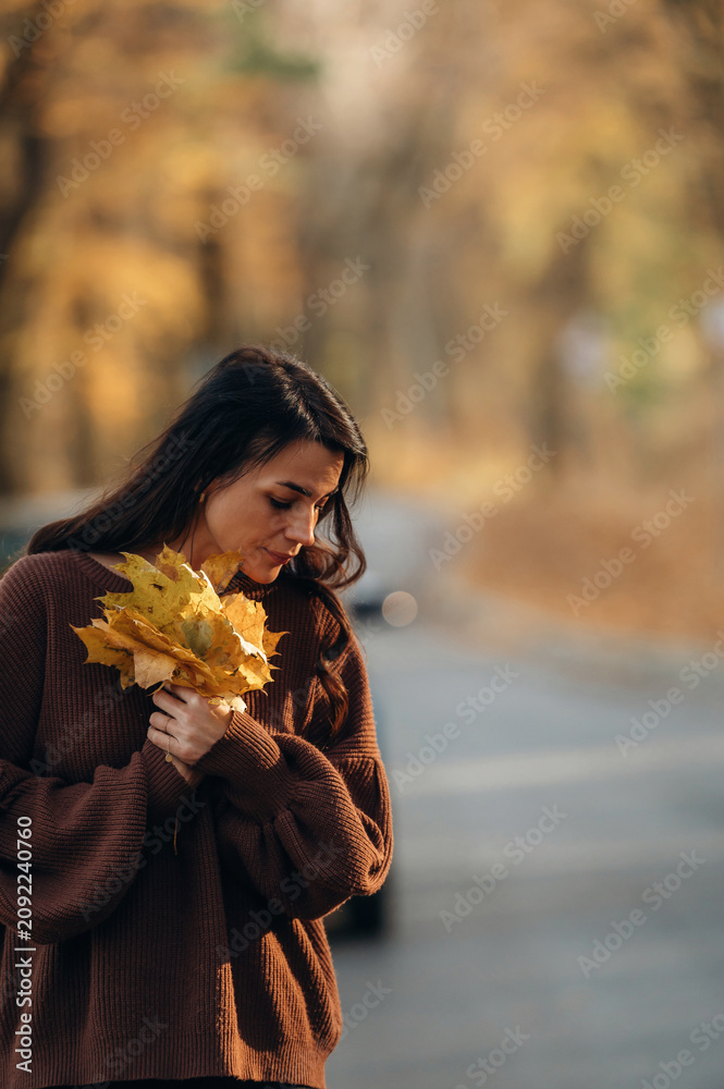 Naklejka premium Fallen leaves in hands. A woman is standing on the asphalt road outdoors at autumn season