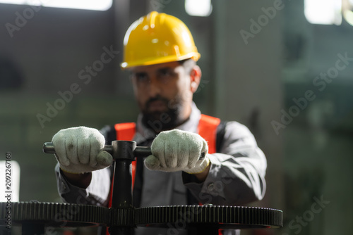 Close-up of technician wearing gloves and hardhat turning valve to operate heavy machinery in industrial factory.