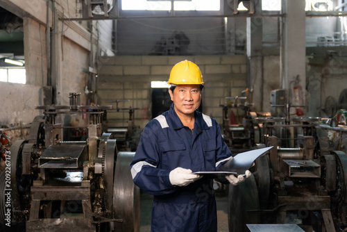 Portrait of confident senior engineer smiling while holding folder report in industrial factory.